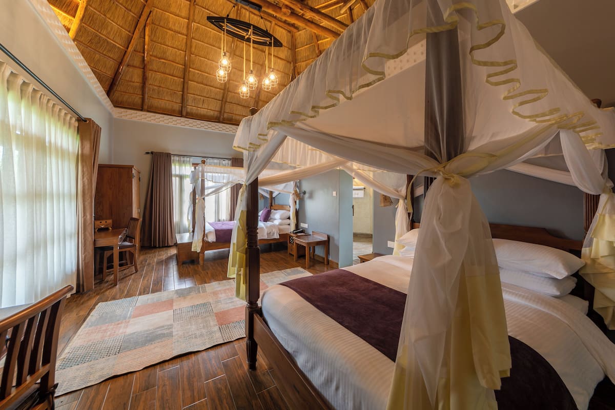 A spacious room with a large bed, wooden flooring, and a high ceiling with exposed beams.