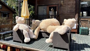 Uma cabana de madeira com varanda, um urso de pelúcia grande e um urso de pelúcia menor.