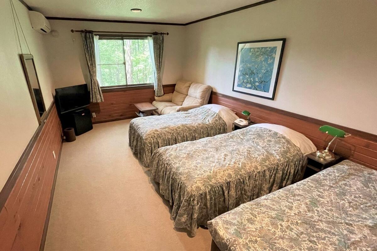 A hotel room with two beds, a television, a small table, a chair, a window with curtains, and a framed picture on the wall.