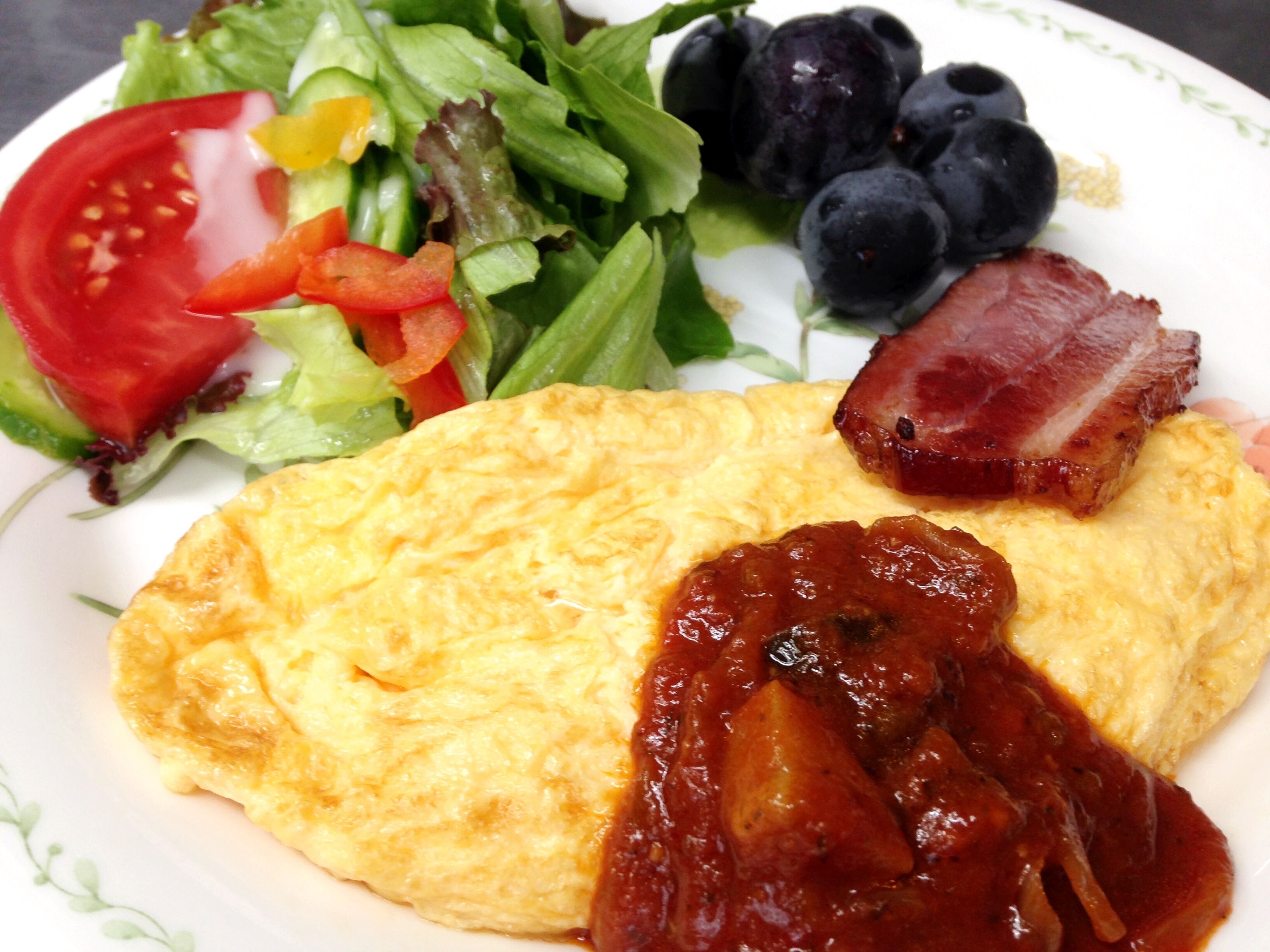A plate with an omelette, bacon, a salad, and blueberries.