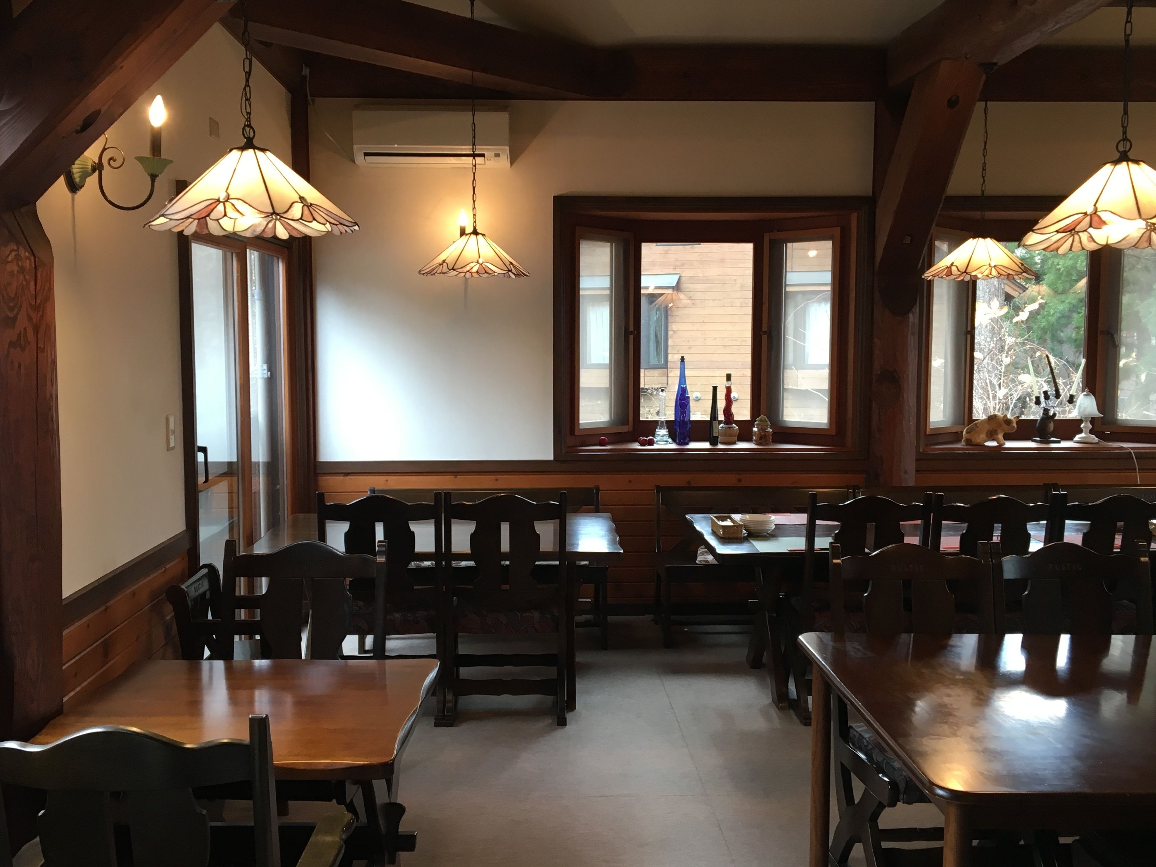 A dining area with wooden tables and chairs, pendant lights, and a window with a view of the outside.