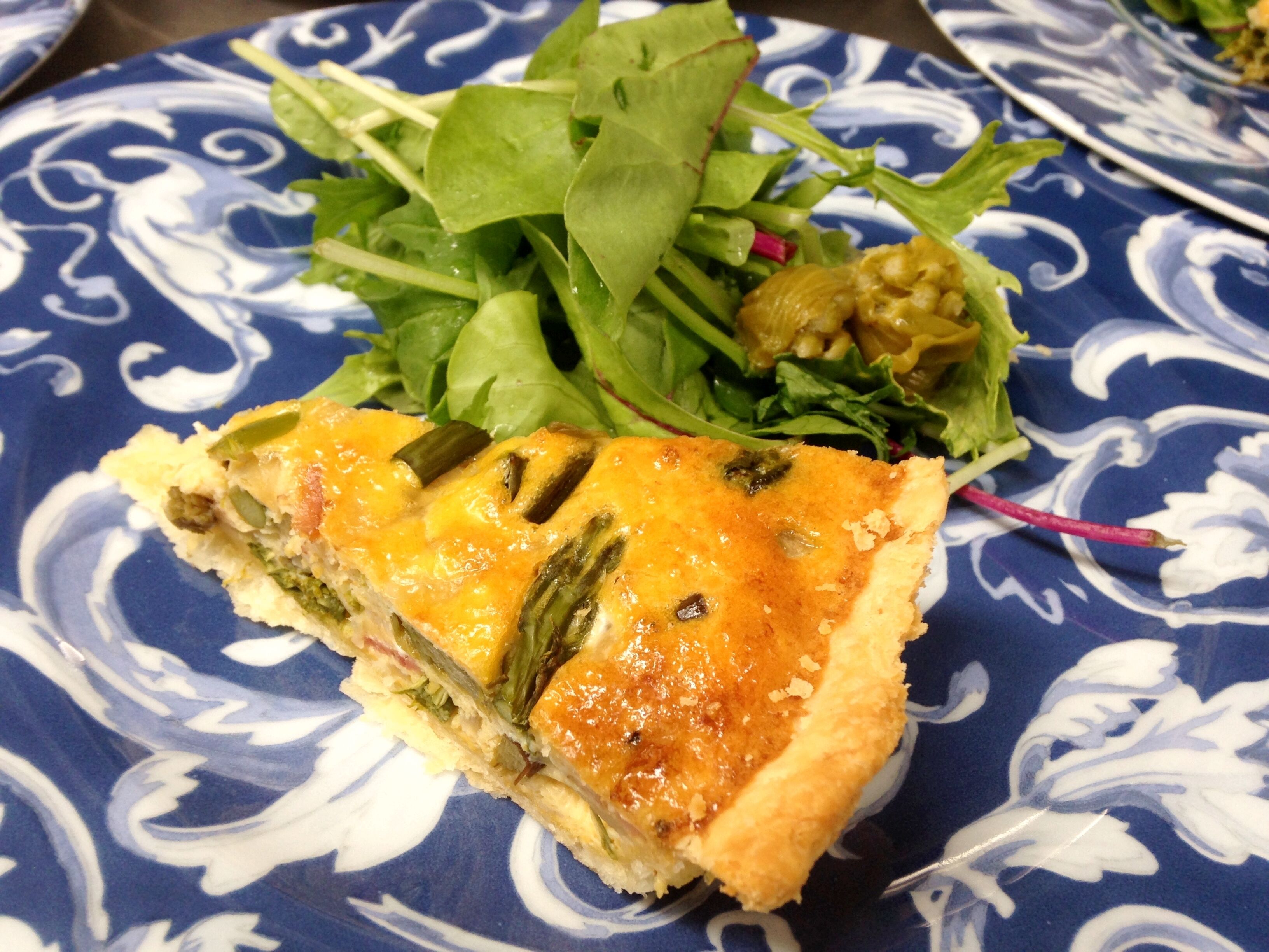 Una porción de quiche sobre un plato con estampado azul y blanco, acompañada de una ensalada.