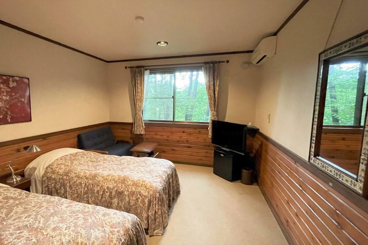 A room with two beds, a chair, a television, and a window with curtains.