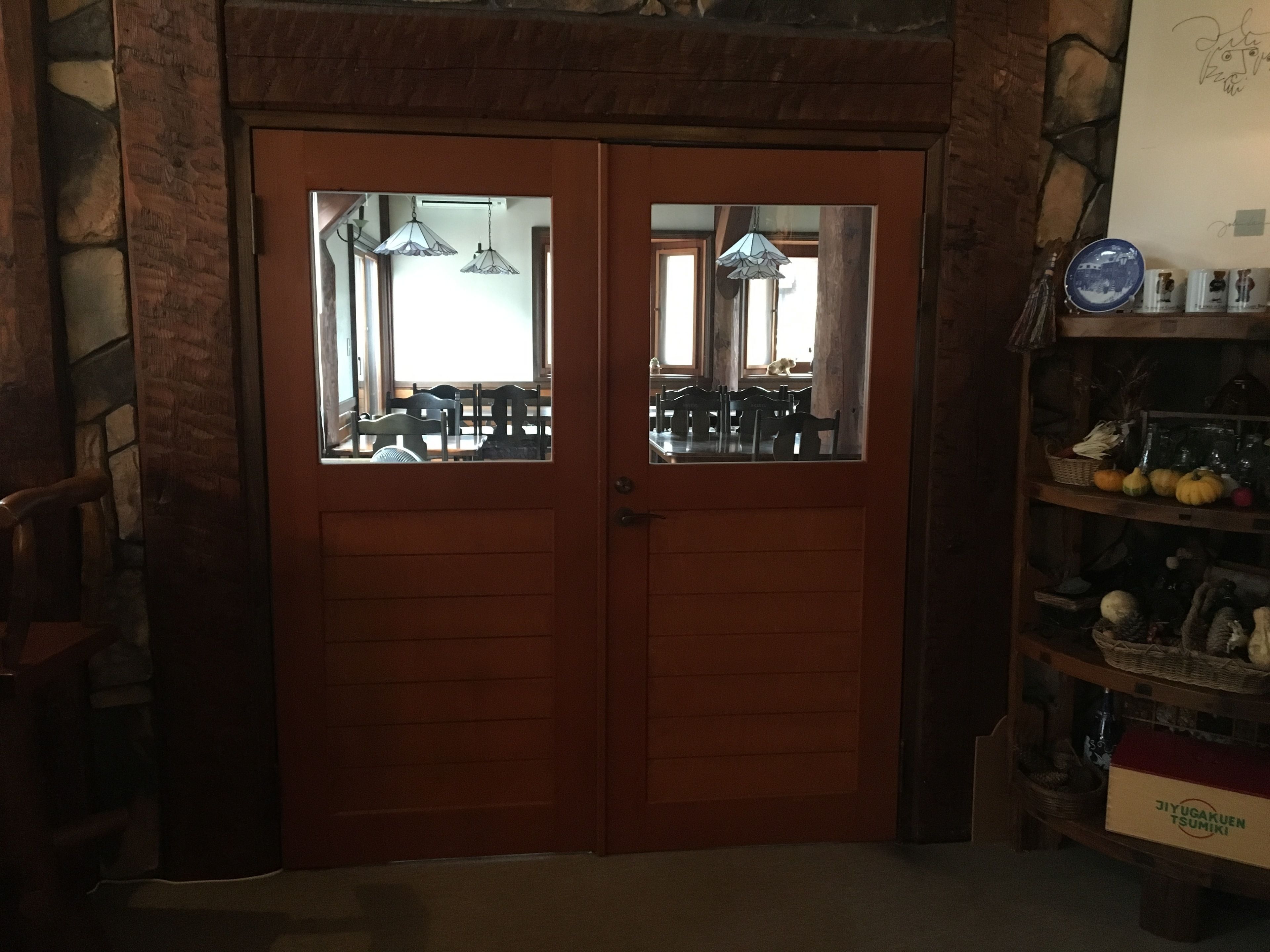 A wooden double door with glass panels, leading to a room with a dining table and chairs, and a shelf with various items.