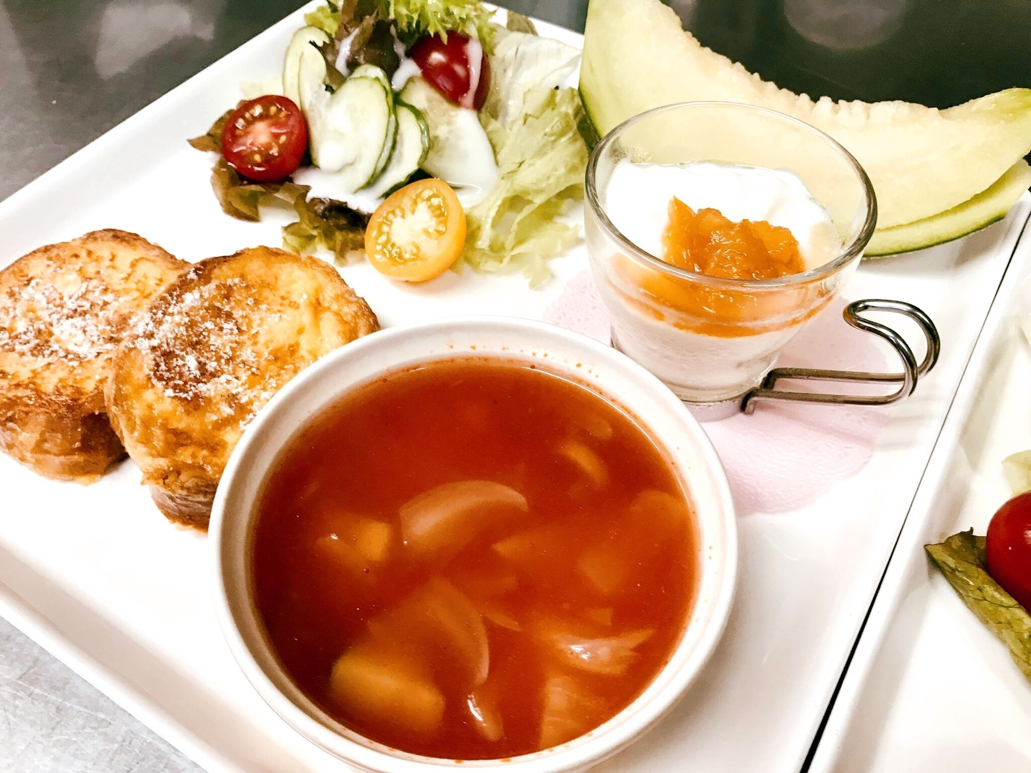 Uma refeição com torradas, sopa, salada e um copo de suco.