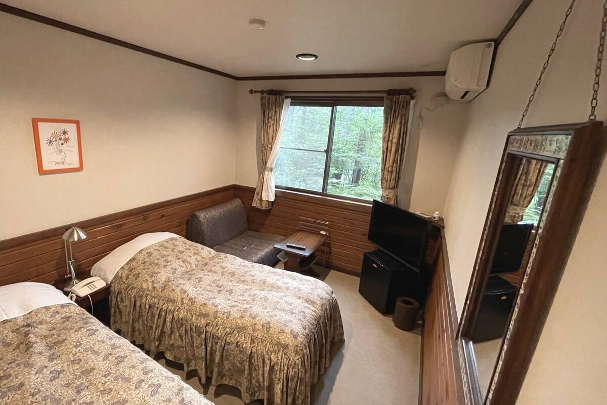 A hotel room with two beds, a desk, a television, and a window with curtains.