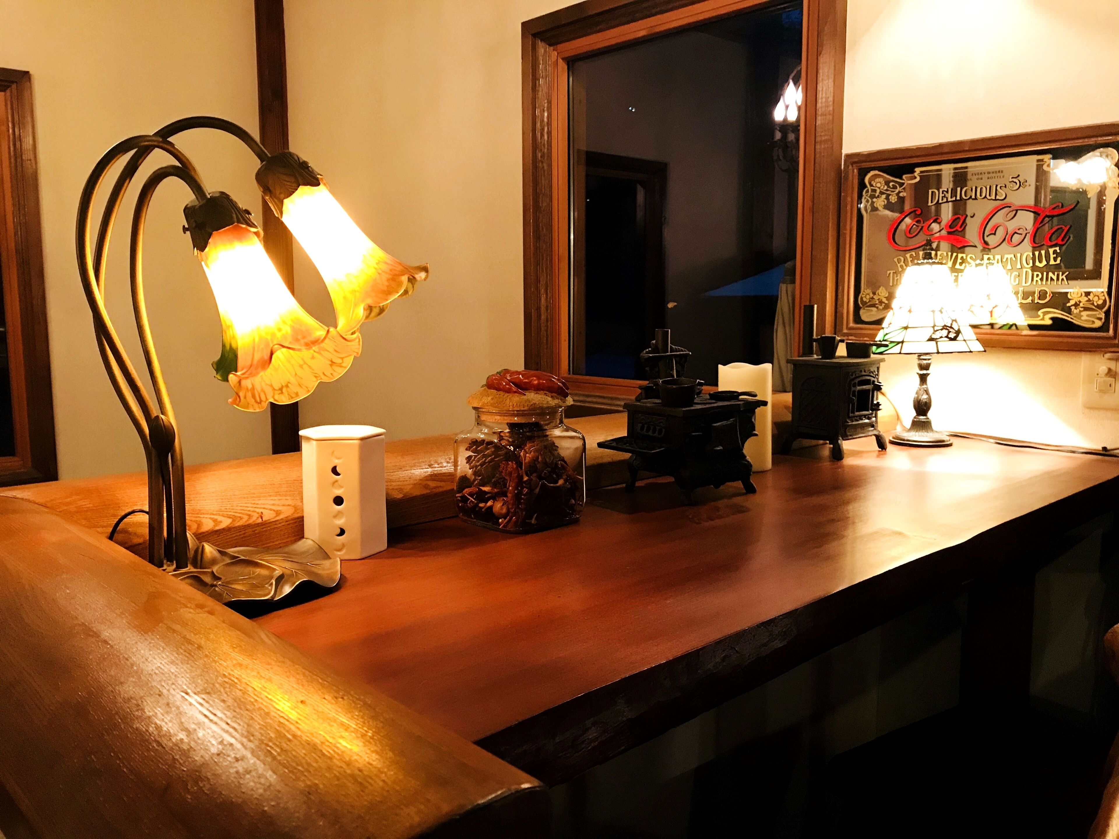 A wooden counter with a vintage-style lamp, a small white candle holder, and a decorative jar with pinecones.