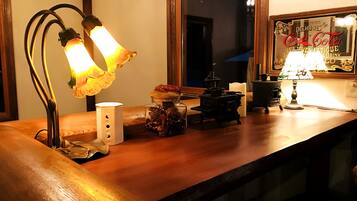 A wooden counter with a vintage-style lamp, a small white candle holder, and a decorative jar with pinecones.