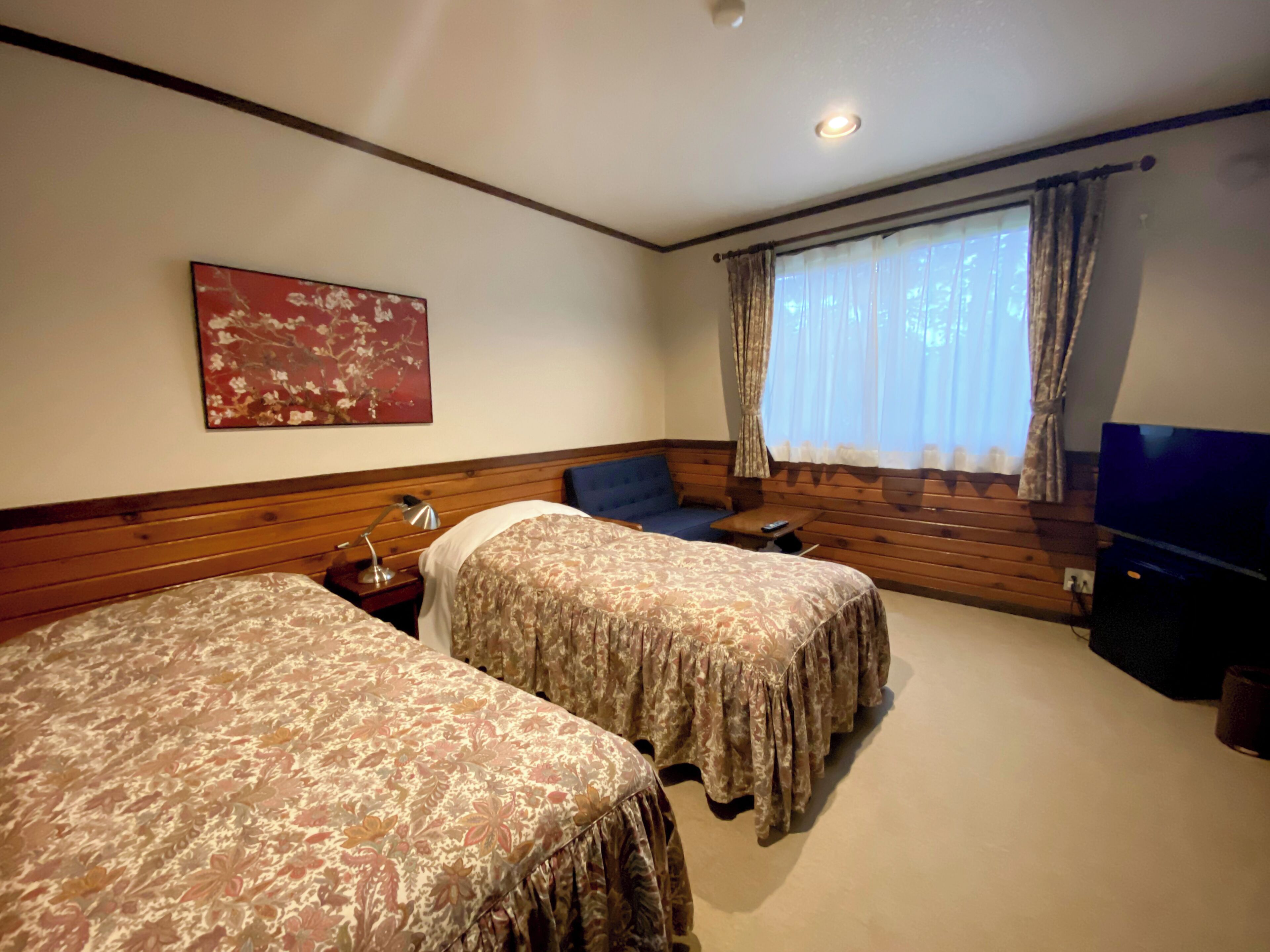 Quarto de hotel com duas camas, televisão, janela com cortinas e um quadro na parede.
