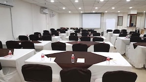 Une salle de conférence équipée de plusieurs tables, de chaises et d’un écran de projection.