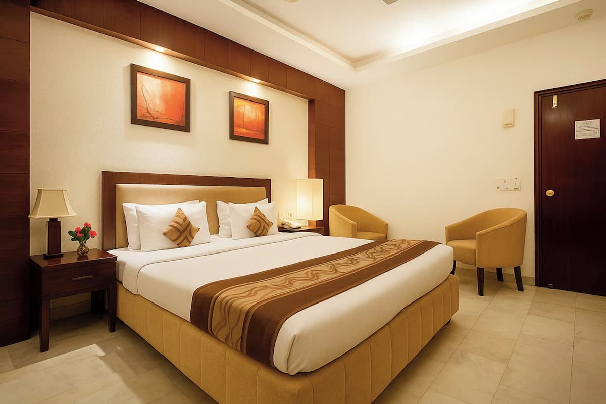 A hotel room with a large bed, two bedside lamps, a chair, and two framed pictures on the wall.
