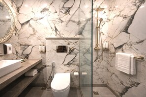 Un bagno moderno con rivestimento in marmo, box doccia in vetro, WC bianco e mobile lavabo con uno specchio grande.
