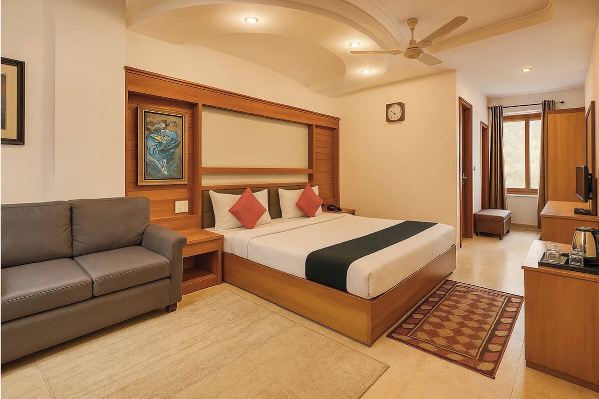 A hotel room with a bed, a sofa, a desk, and a ceiling fan.
