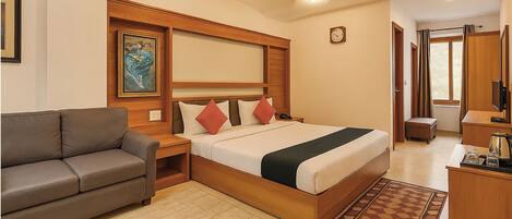 A hotel room with a bed, a sofa, a desk, and a ceiling fan.