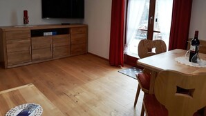 Un salon avec un meuble en bois, un téléviseur, une table à manger avec des chaises et une fenêtre ornée de rideaux rouges.