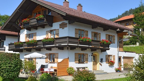 Il s’agit d’un bâtiment de style chalet traditionnel, doté d’un toit en pente, de balcons en bois ornés de jardinières et d’un jardin bien entretenu.