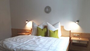 Un lit bien fait, avec une literie blanche et des oreillers verts, deux tables de chevet avec des lampes, et une petite table de nuit en bois avec un tiroir.