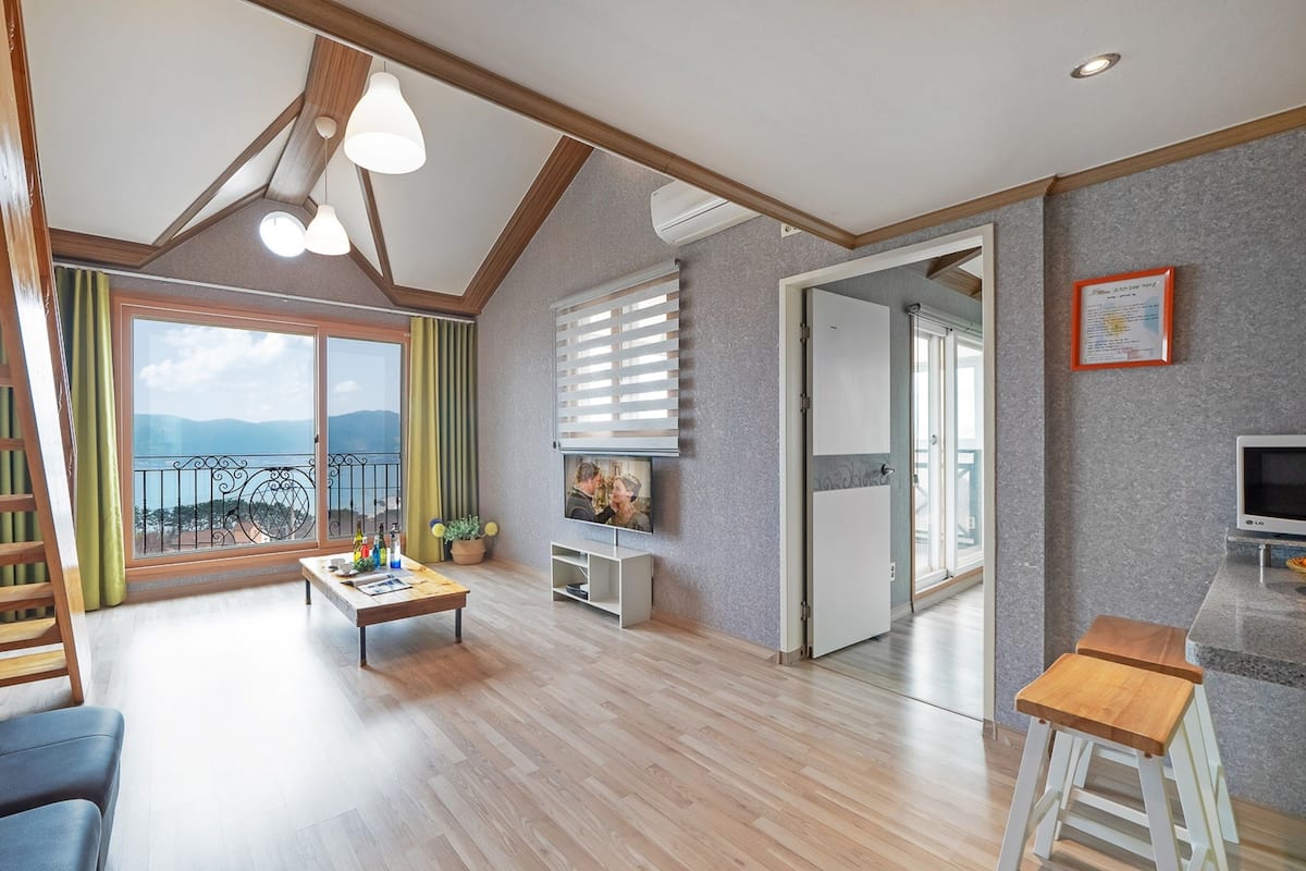Un salón espacioso con suelo de madera, un sofá, una mesa de centro, un televisor y un balcón con vistas a las montañas.