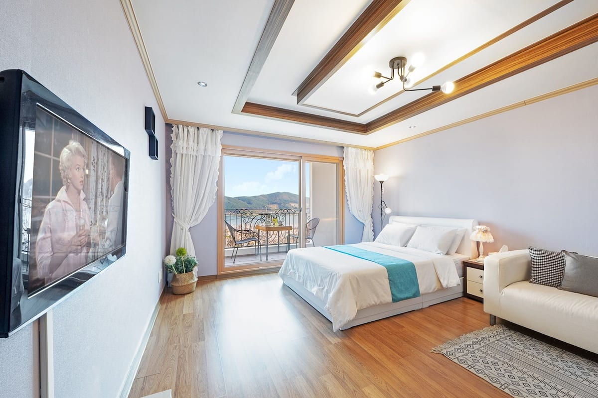 Una habitación de hotel moderna con una cama grande, un sofá, un televisor y un balcón con vistas a las colinas.