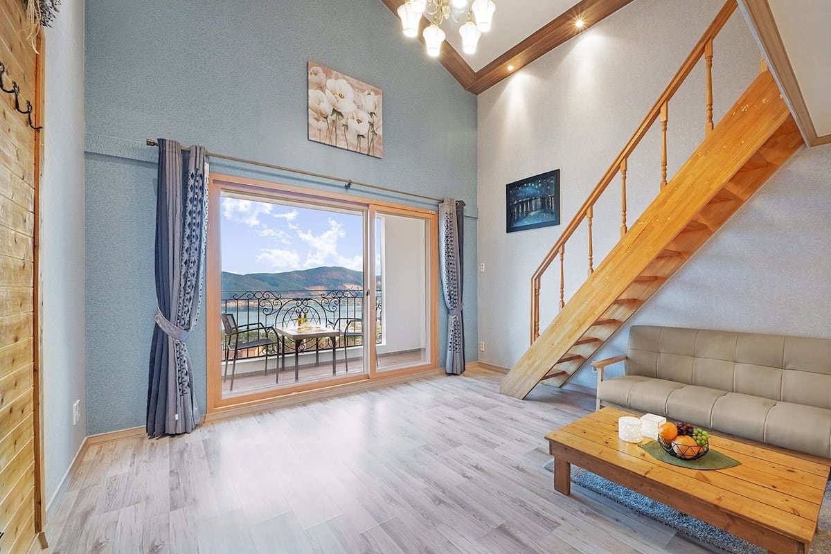 Un salón espacioso con una escalera de madera, un sofá y un balcón con vistas al mar.