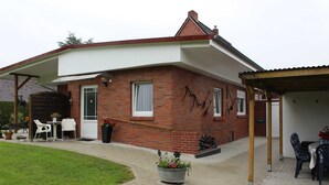Una casa de ladrillo con un porche cubierto, mobiliario exterior y un jardín.
