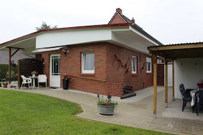 Una casa de ladrillo con un porche cubierto, mobiliario exterior y un jardín.