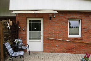 A patio with a brick wall, a white door, and a window. There is a table with chairs and a small potted plant.
