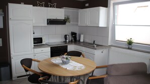 Cocina compacta con gabinetes blancos, una mesa de comedor con sillas, microondas, cafetera y ventana con vistas.