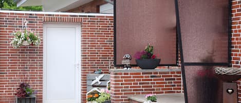 A brick building with a white door, steps leading to a porch, and various potted plants.