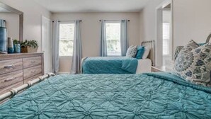 Une chambre à coucher comprenant un lit, une commode, un ventilateur de plafond et deux fenêtres avec des rideaux.