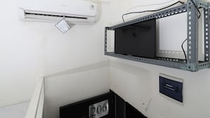 A room with a mounted air conditioner, a metal-framed shelf, and a numbered door.