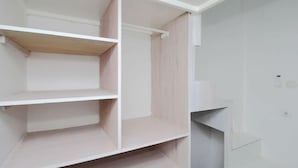 A room with white walls and a wooden floor. There are three white shelves and a white door.