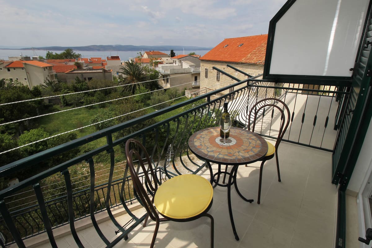 A balcony with a table and chairs, overlooking a coastal area with houses and a body of water.