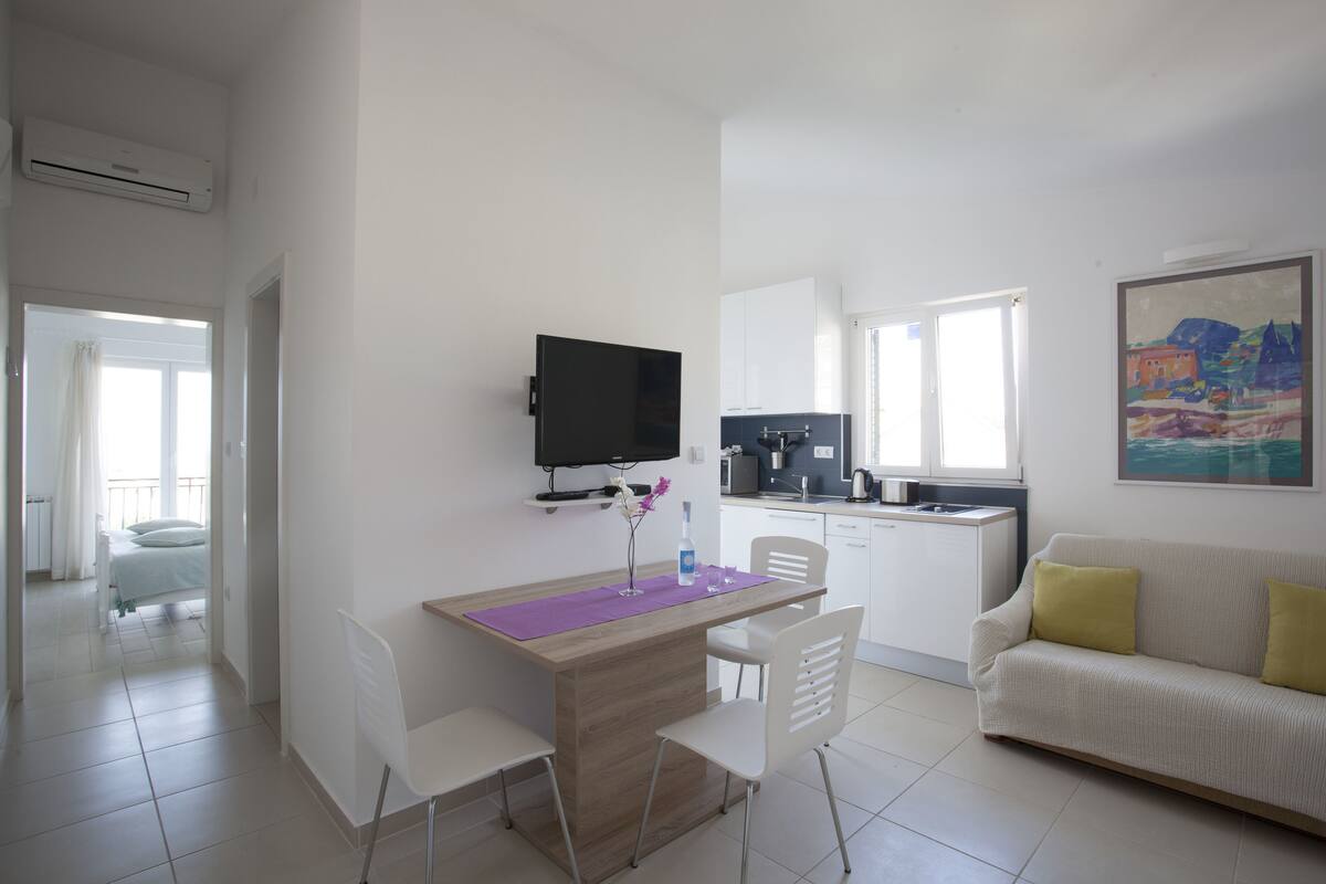 A modern, well-lit room with a dining area, a sofa, and a kitchen.