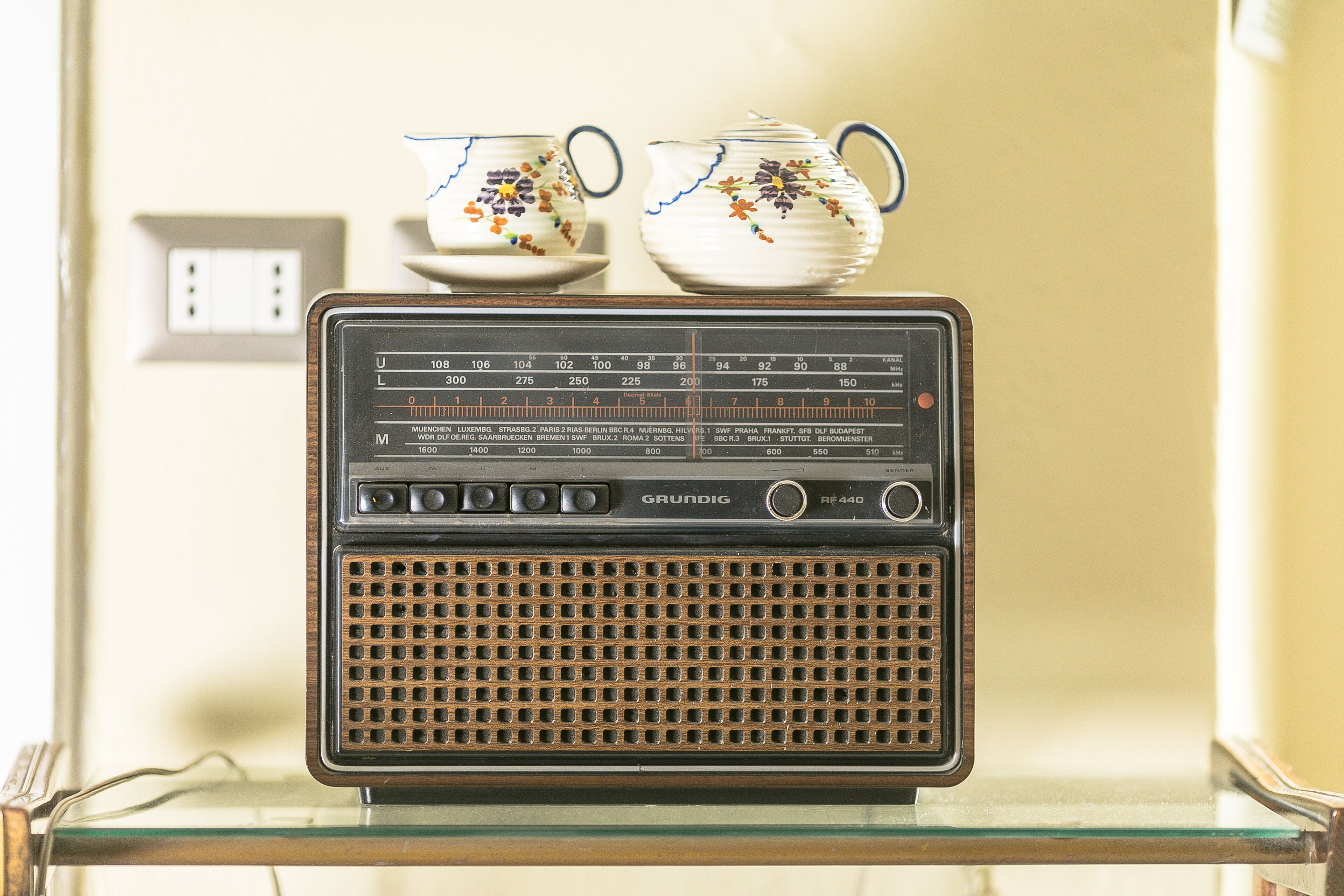 Un aparell de ràdio Grundig antic sobre una superfície de vidre, amb dues tasses de ceràmica decoratives a sobre.
