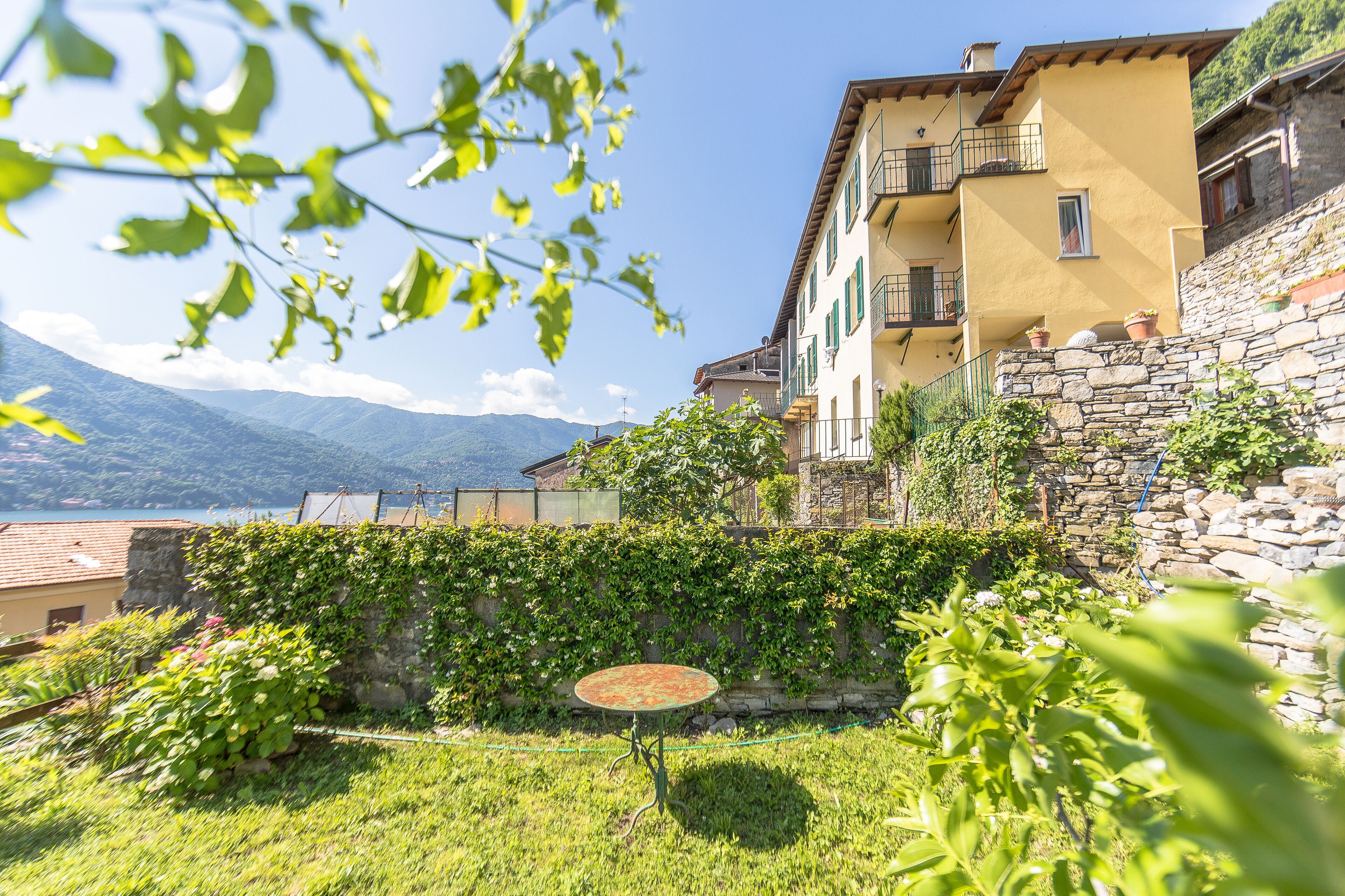 A hillside building with a stone wall, a small table, and lush greenery.