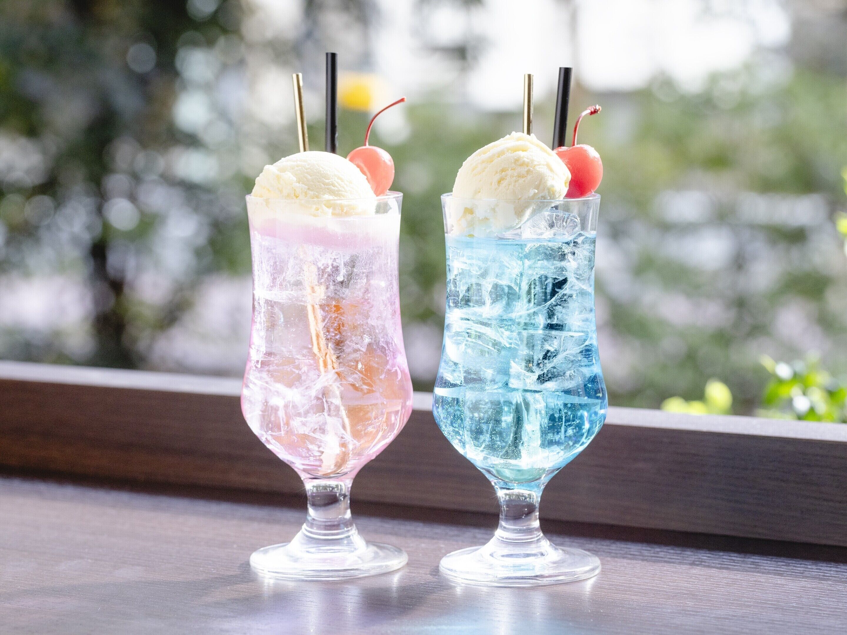 Deux verres de crème glacée, avec des pailles et des cerises, sont posés sur une table près d’une fenêtre.