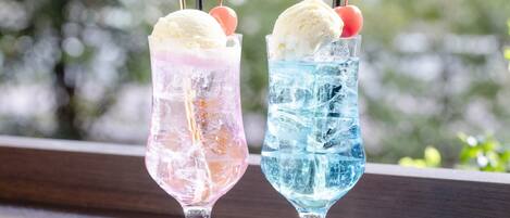 Two glasses of ice cream with straws and cherries on a table by a window.