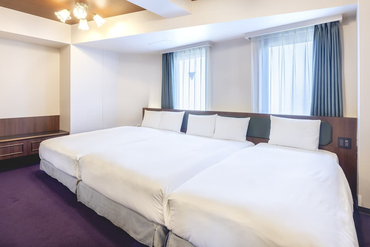 A hotel room with a large bed, a wooden headboard, a bedside table, and a window with curtains.