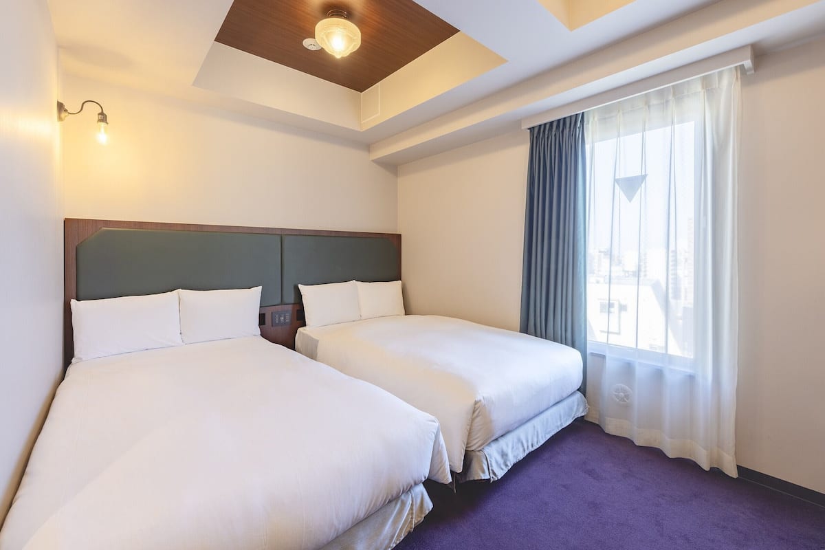 A hotel room with two beds, a wooden ceiling, a window with curtains, and a purple carpet.