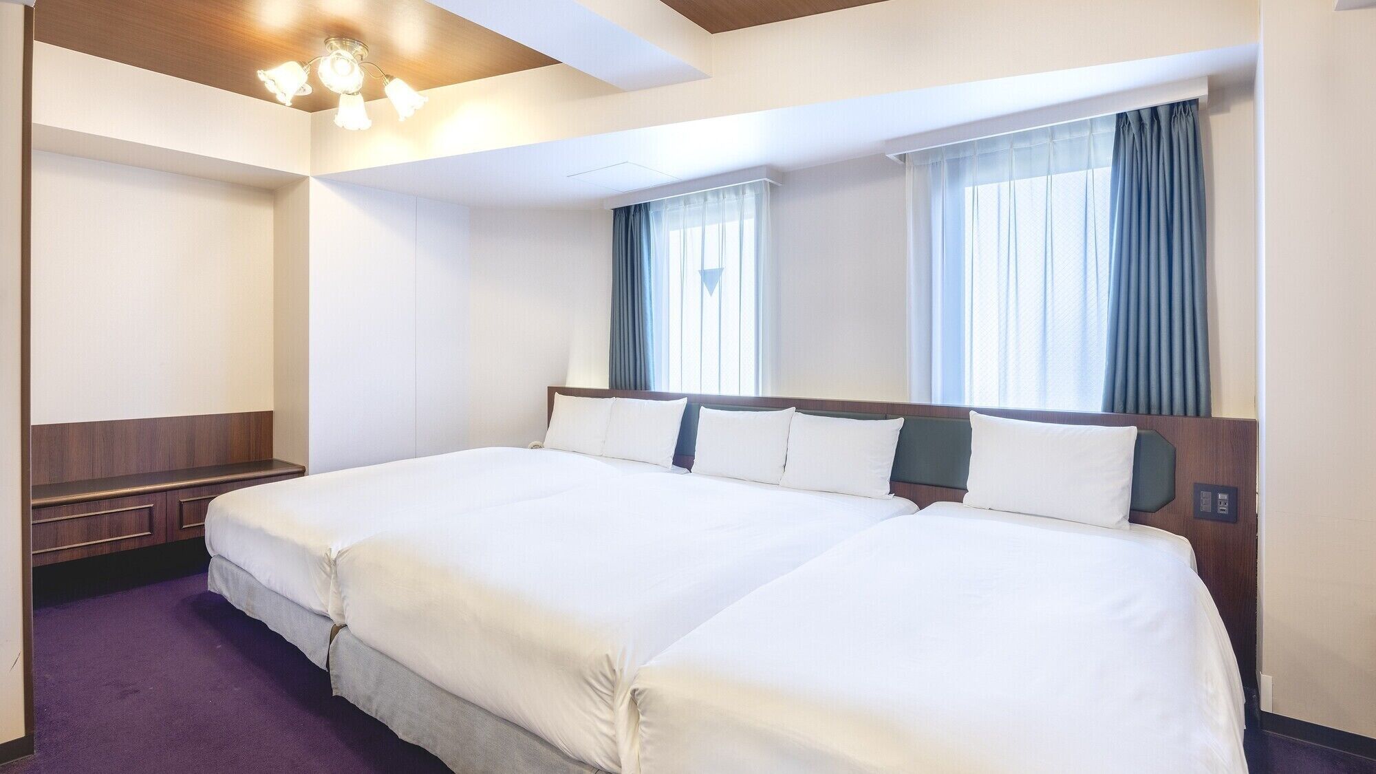 Une chambre d’hôtel avec deux lits, une tête de lit en bois, une banquette intégrée et un luminaire au plafond.