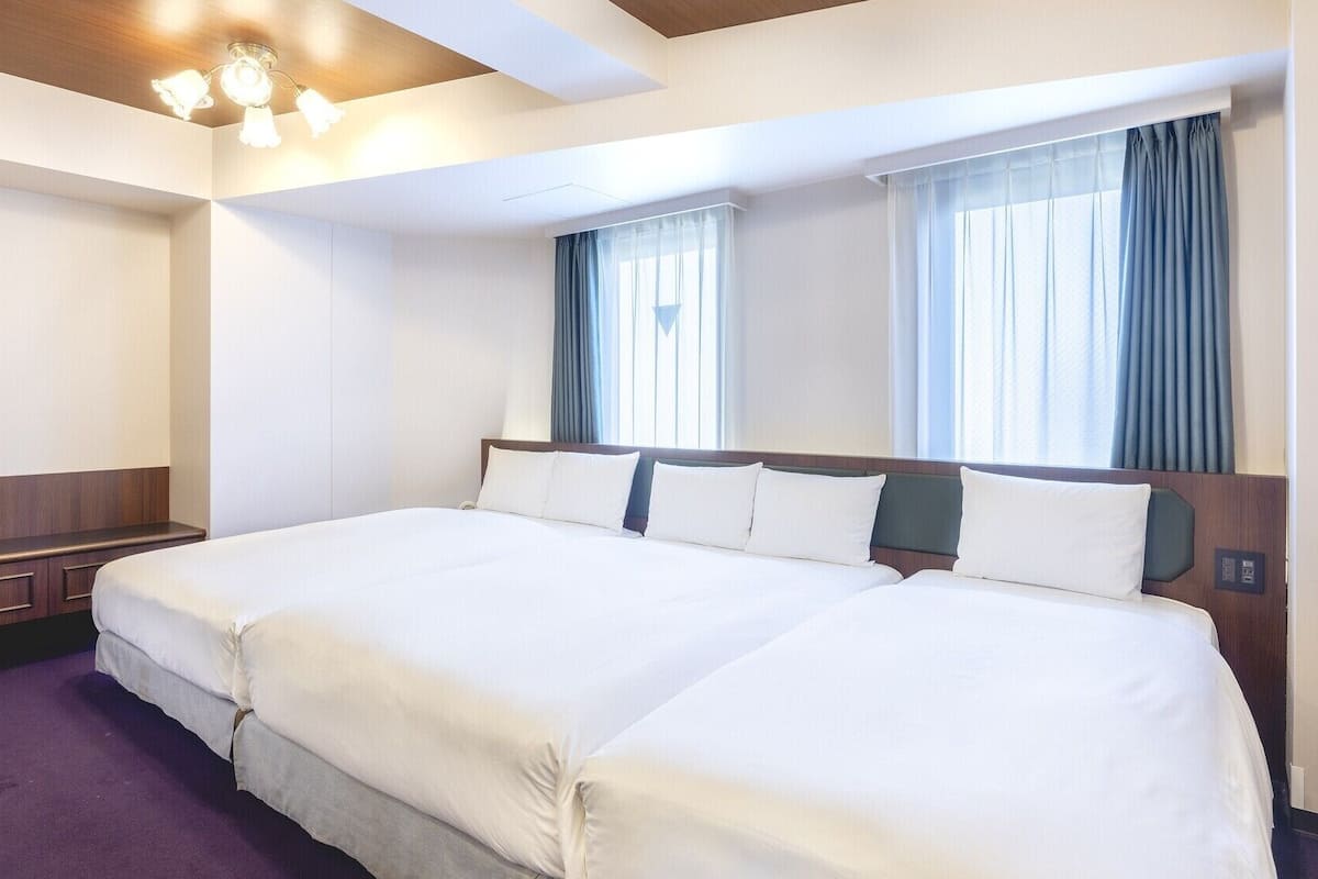 A hotel room with two beds, a wooden headboard, a built-in bench, and a ceiling light fixture.