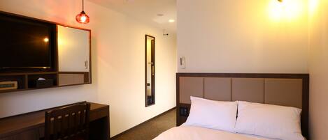 A hotel room with a bed, a desk, a chair, a TV, an air conditioner, and a wall-mounted light.