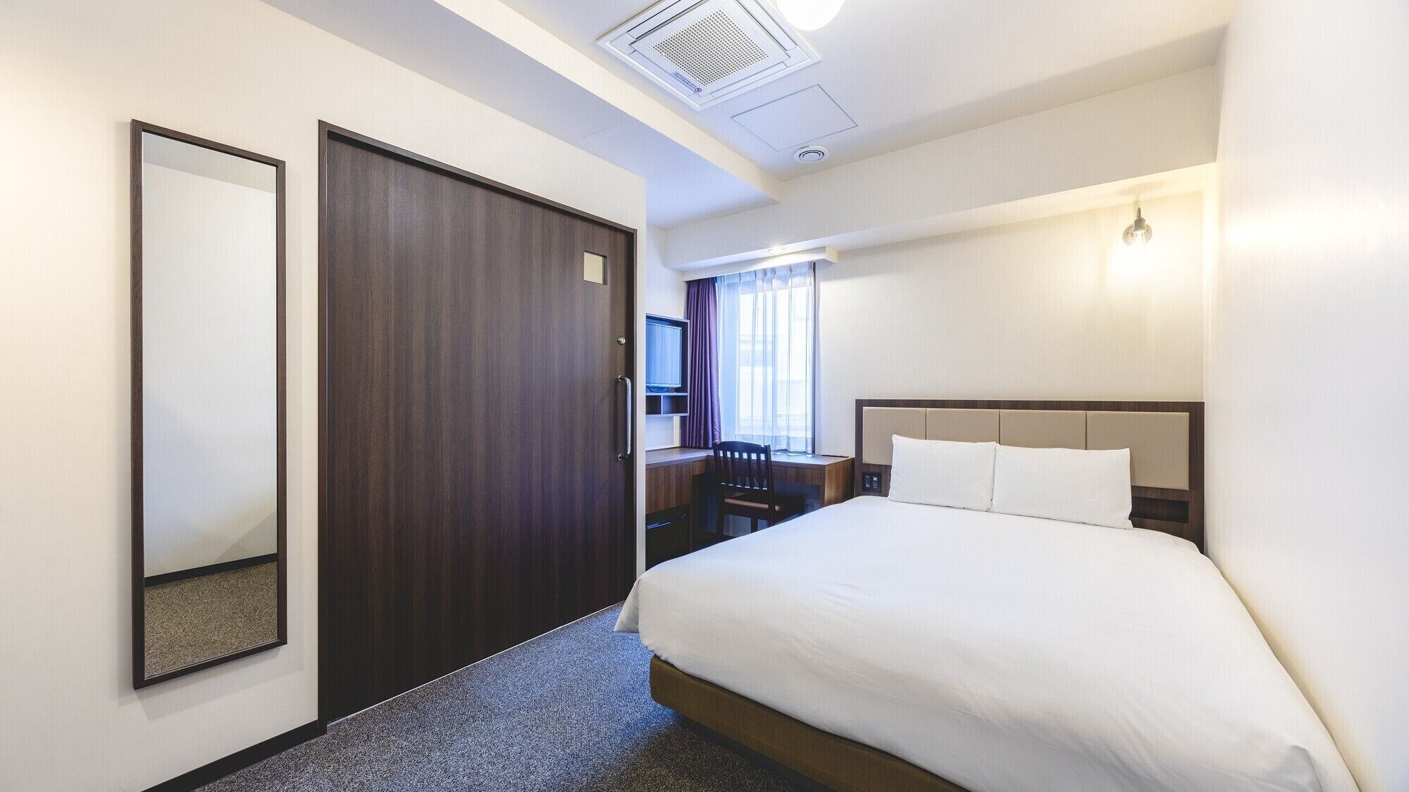 Une chambre d’hôtel équipée d’un lit, d’un bureau, d’une chaise, d’une télévision et d’une fenêtre avec des rideaux.