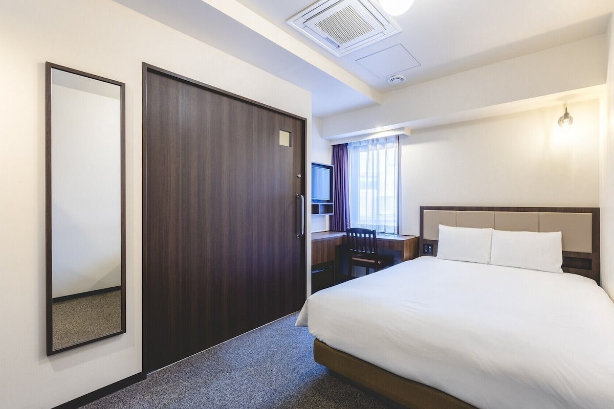 A hotel room with a bed, a desk, a chair, a TV, and a window with curtains.
