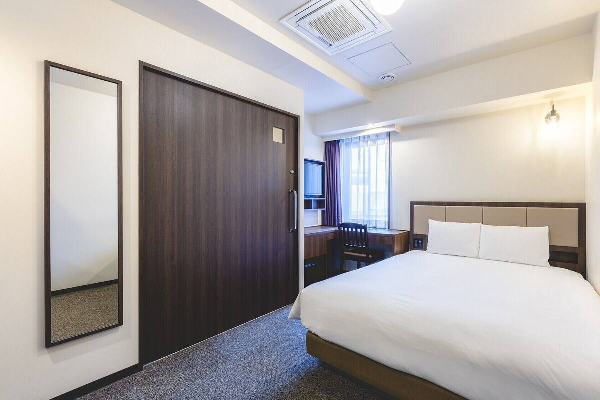 Une chambre d’hôtel équipée d’un lit, d’un bureau, d’une chaise, d’une télévision et d’une fenêtre avec des rideaux.