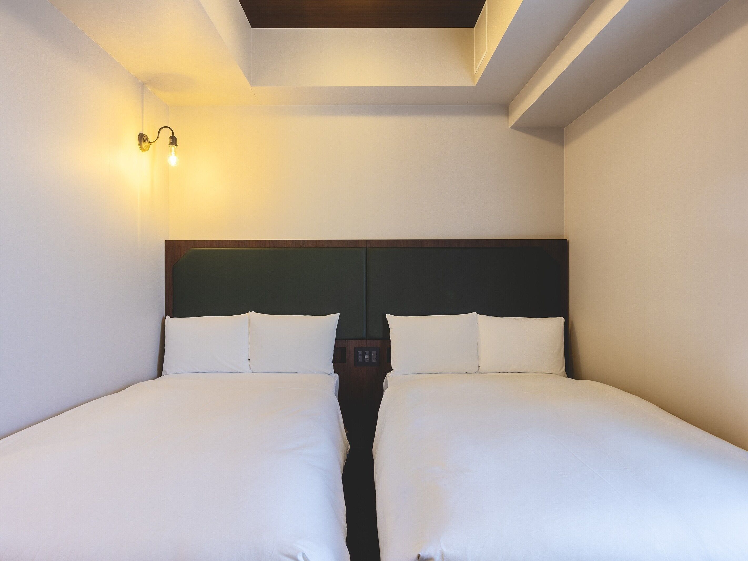 A double bed with white linens in a hotel room with a skylight and a wall-mounted light fixture.