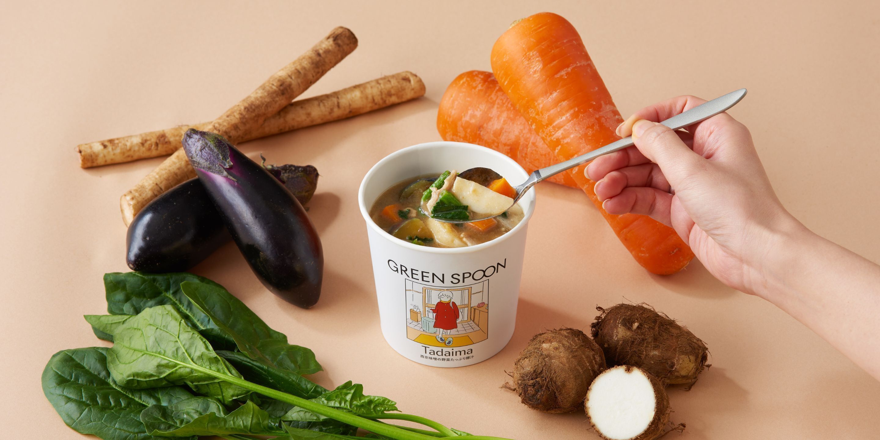 Une main tenant une cuillère au-dessus d’un bol sur lequel est écrit « CUILLÈRE VERTE », et qui contient des légumes et une carotte.