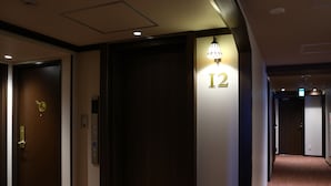 A hotel corridor with a closed elevator door, a wall-mounted sign indicating room number 12, and a carpeted floor. - KOKO HOTEL Ikebukuro (Tokyo)