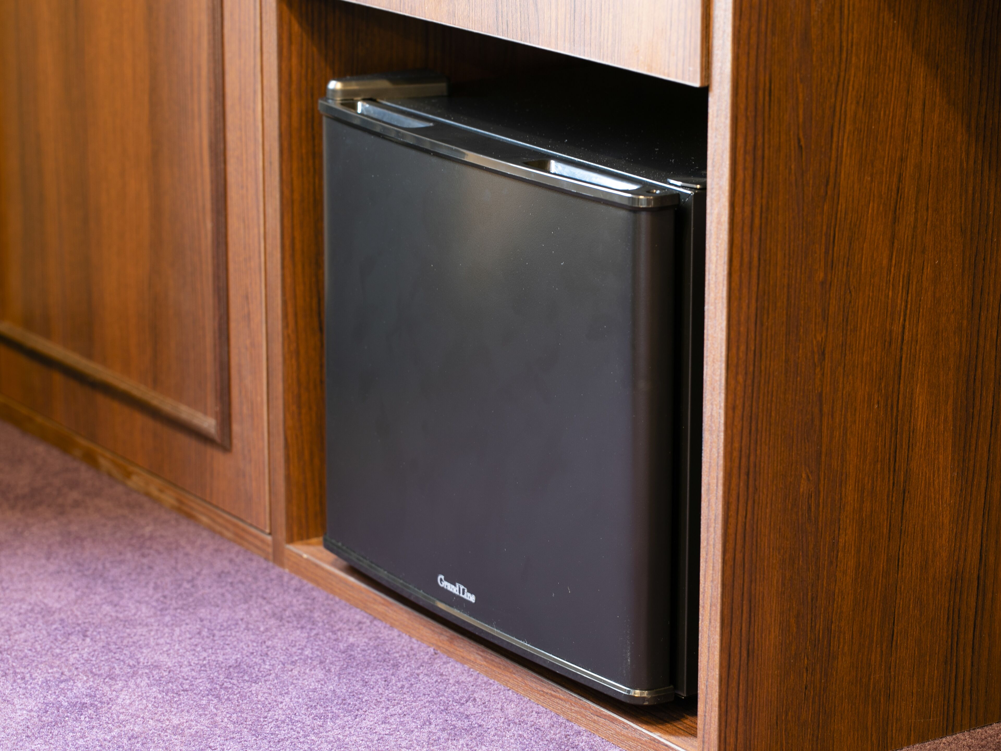 Un frigorifero nero in una cucina con pensili in legno e un tappeto viola.